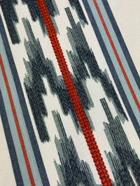 close up of fabric featuring a striped pattern with embroidery in blue and red colors.