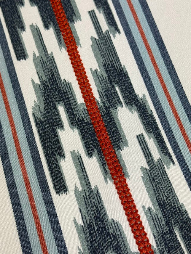 close up of fabric featuring a striped pattern with embroidery in blue and red colors.