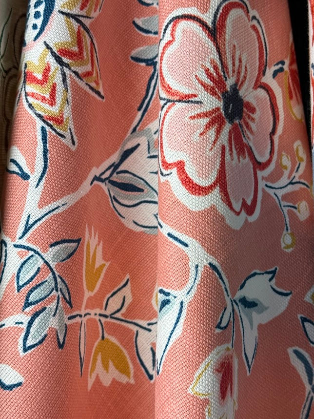 Close-up of floral fabric with pink, red, and white flowers on a coral background