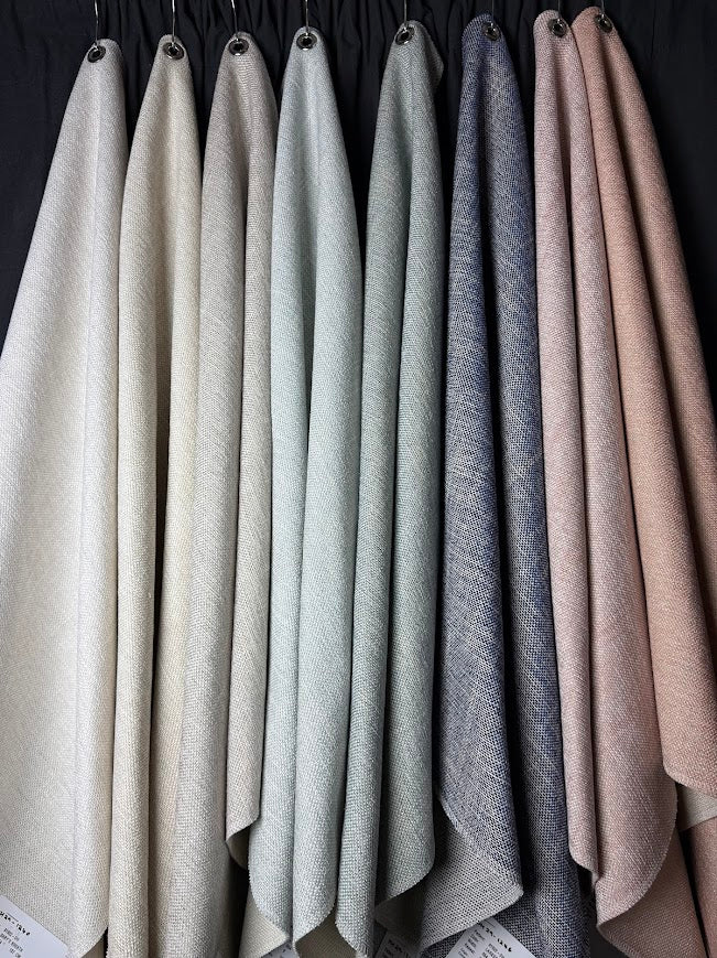 Set of fabric swatches in various neutral colors hanging against a dark background.